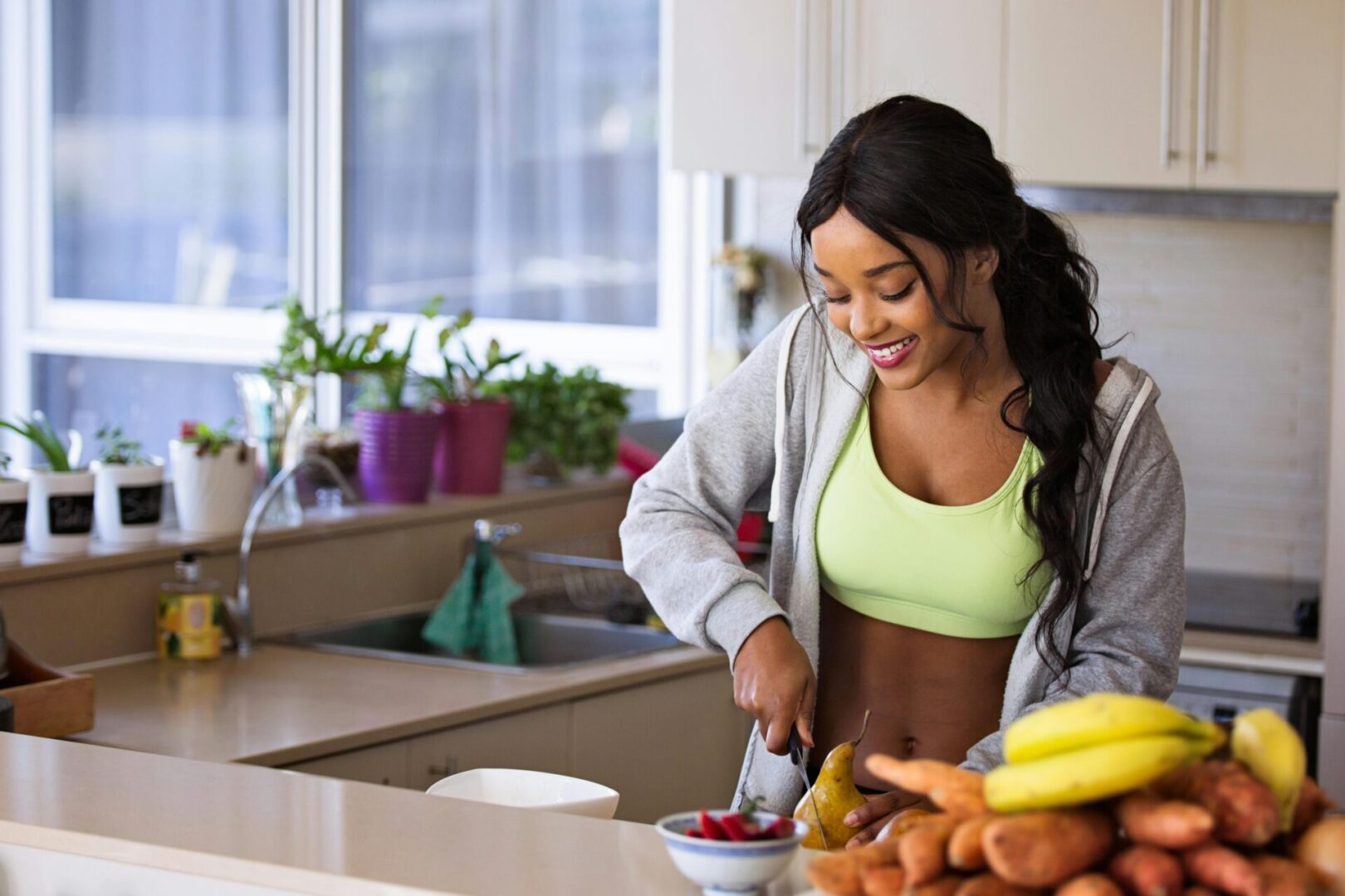 A woman cutting fruit in the kitchen with bananas and carrots.