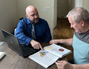 Two men sitting at a table with papers and a laptop.